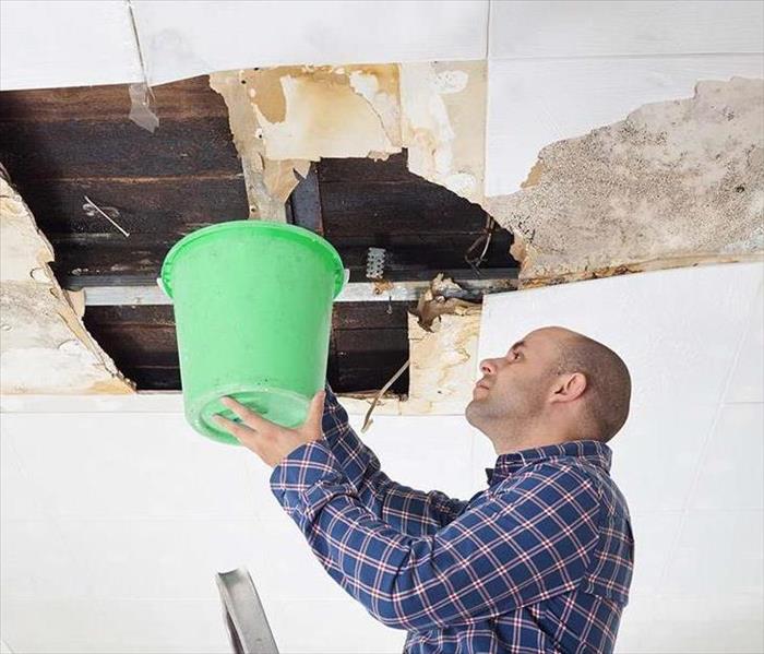 Man holding bucket near ceiling of home in Columbia SC that was negatively affected by storm related water damage